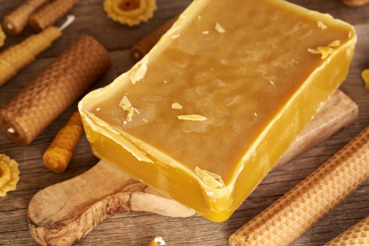 A block of bees wax with handmade candles on a table