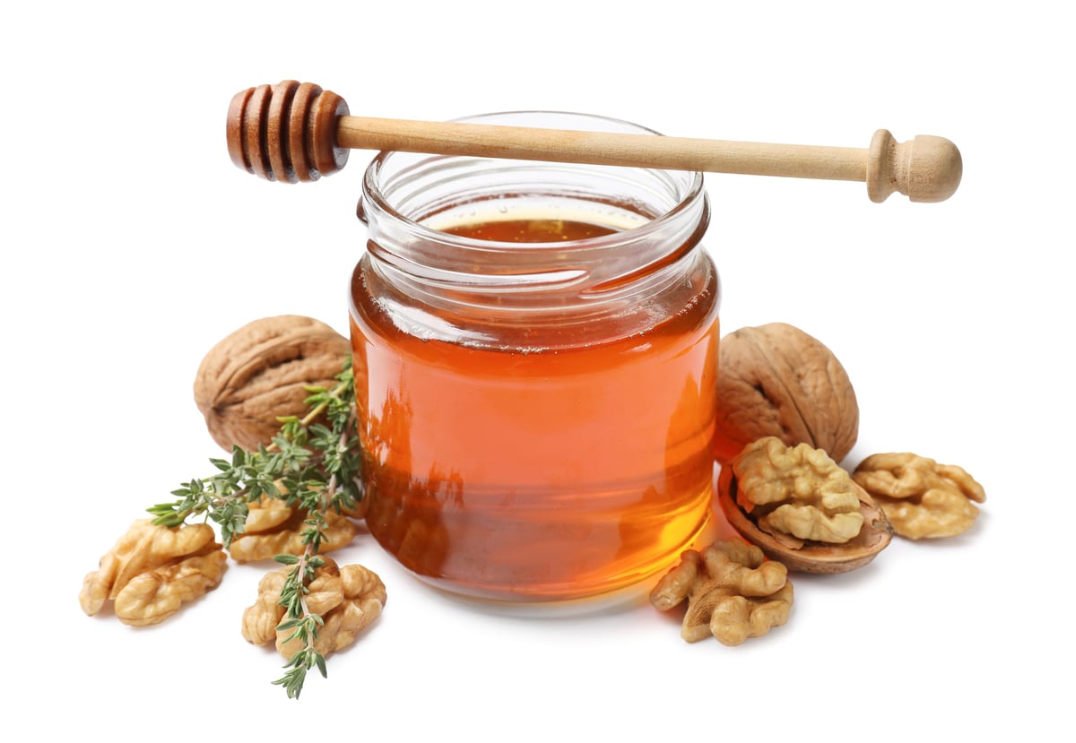 Honey with walnuts, thyme and dipper isolated on white